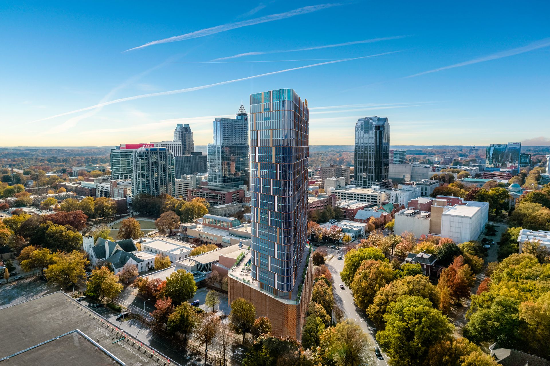 Aerial 3D rendering of the VeLa mixed-use tower in Raleigh by day, a colorful gridded facade rising above the downtown skyline and surrounding tree canopy.