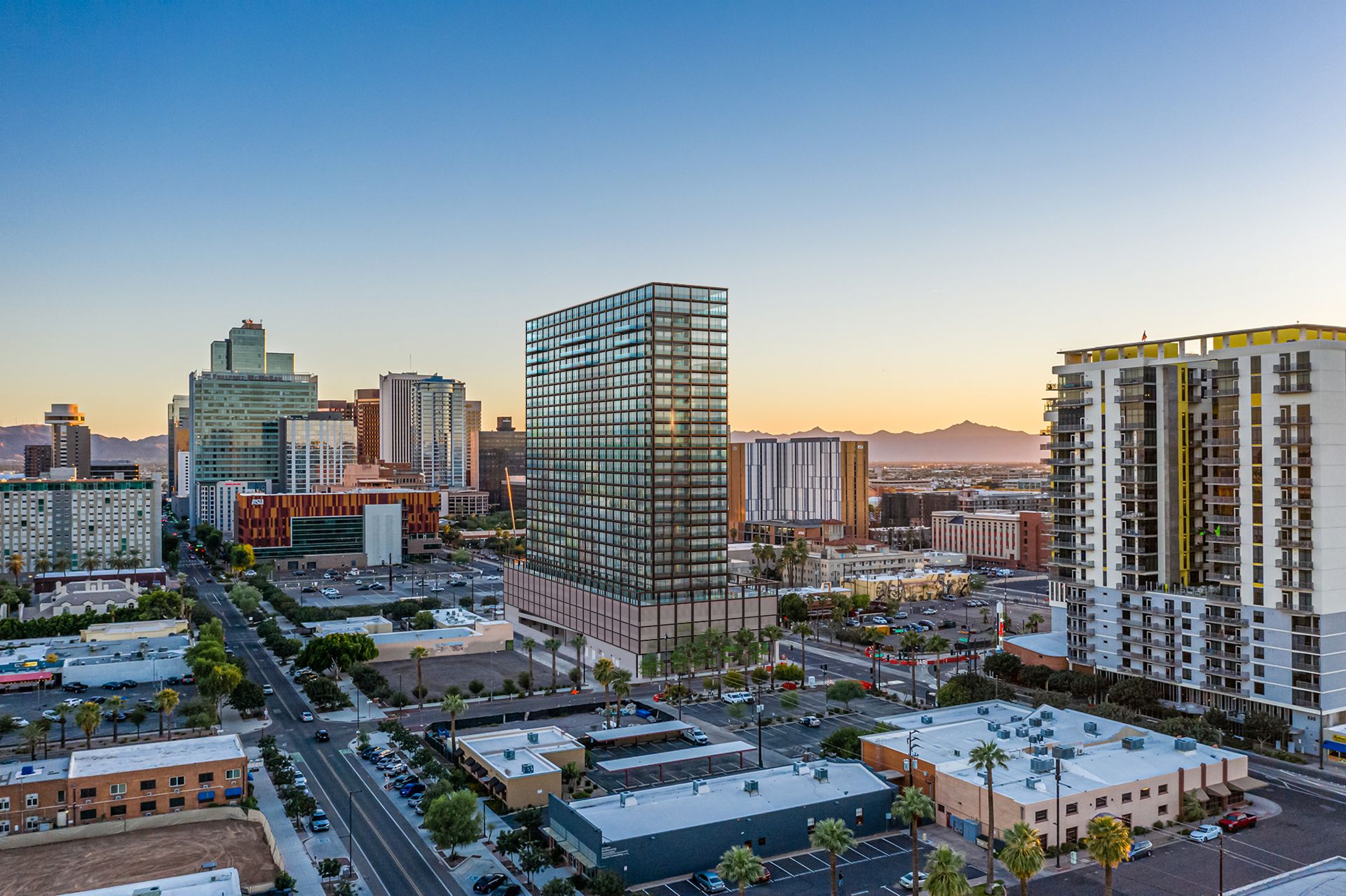 Aerial 3D rendering of the VeLa gridded glass tower in downtown Phoenix at dusk, with the city grid below and mountains on the horizon.